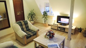 A cozy living room with a plaid armchair, a coffee table with a vase of flowers, a television on a stand, and a potted plant. - Apartment in Swinoujscie Near Baltic Beach (Swinoujscie)