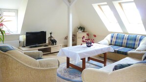 A cozy living room with a sofa, armchairs, a TV, and a table with a vase. - Apartment in Swinoujscie Near Baltic Beach (Swinoujscie)