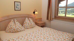 A bedroom with a bed, a nightstand, a lamp, a window with curtains, and a framed picture on the wall. - Apartment in Krimml With Balcony (Krimml)
