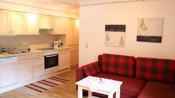 Un espacio habitable compacto con kitchenette, un sofá rojo a cuadros y una pequeña mesa blanca.