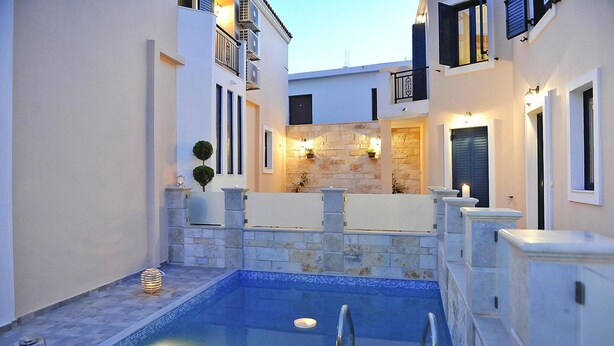 A swimming pool with stone walls and a metal railing, surrounded by buildings with balconies and windows. - Panormo Apartment Near the Sea (Mylopotamos)