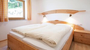 Een houten bed met hoofdeinde, een nachtkastje en een raam met gordijnen.