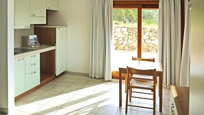 A kitchen with a dining area, a stone wall outside, and a window with curtains. - Apartment in Sardinia Near Surfing Paradise (Palau)