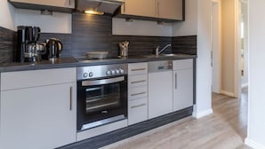 A modern kitchen with grey cabinets, a built-in oven, a coffee maker, and a sink. - Ferienwohnung Strandperle (St. Peter-Ording)