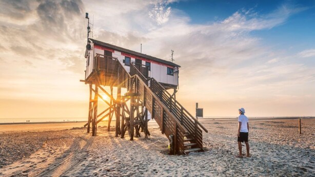 A lifeguard tower on a beach with a person standing nearby. - Ferienwohnung Strandperle (St. Peter-Ording)
