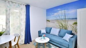 A living room with a blue sofa, a round coffee table, and a dining table with chairs. - Cozy Holiday Studio, Close to the Beach (Kołobrzeg)