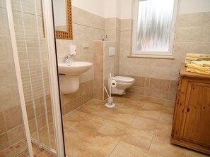 Een badkamer met douche, wastafel, toilet en een houten kast.