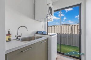 A modern kitchen with a built-in sink, a compact dishwasher, and a window overlooking a backyard. - Marina Views - Echuca Holiday Homes (Moama)