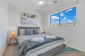 A bedroom with a bed, a nightstand, a lamp, a window with a view of the sky, and a painting on the wall. - Marina Views (Moama)