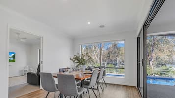 Un coin repas avec une table dressée pour quatre personnes, des chaises, une plante et une vue sur les arbres et une piscine.