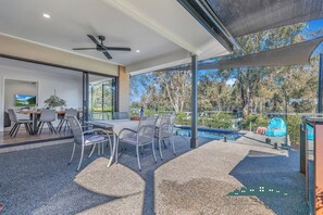 A modern outdoor dining area with a pool, a ceiling fan, and a view of the surrounding trees. - Marina Views (Moama)
