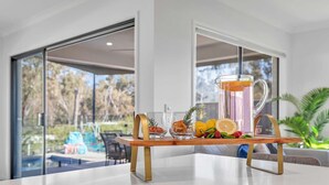 A modern dining area with a glass table, a pitcher of orange juice, and fresh fruits. - Marina Views (Moama)