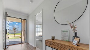 Un intérieur moderne avec une porte-fenêtre coulissante donnant sur un balcon, une console en bois ornée d’un vase et d’un objet encadré, et un miroir fixé au mur.