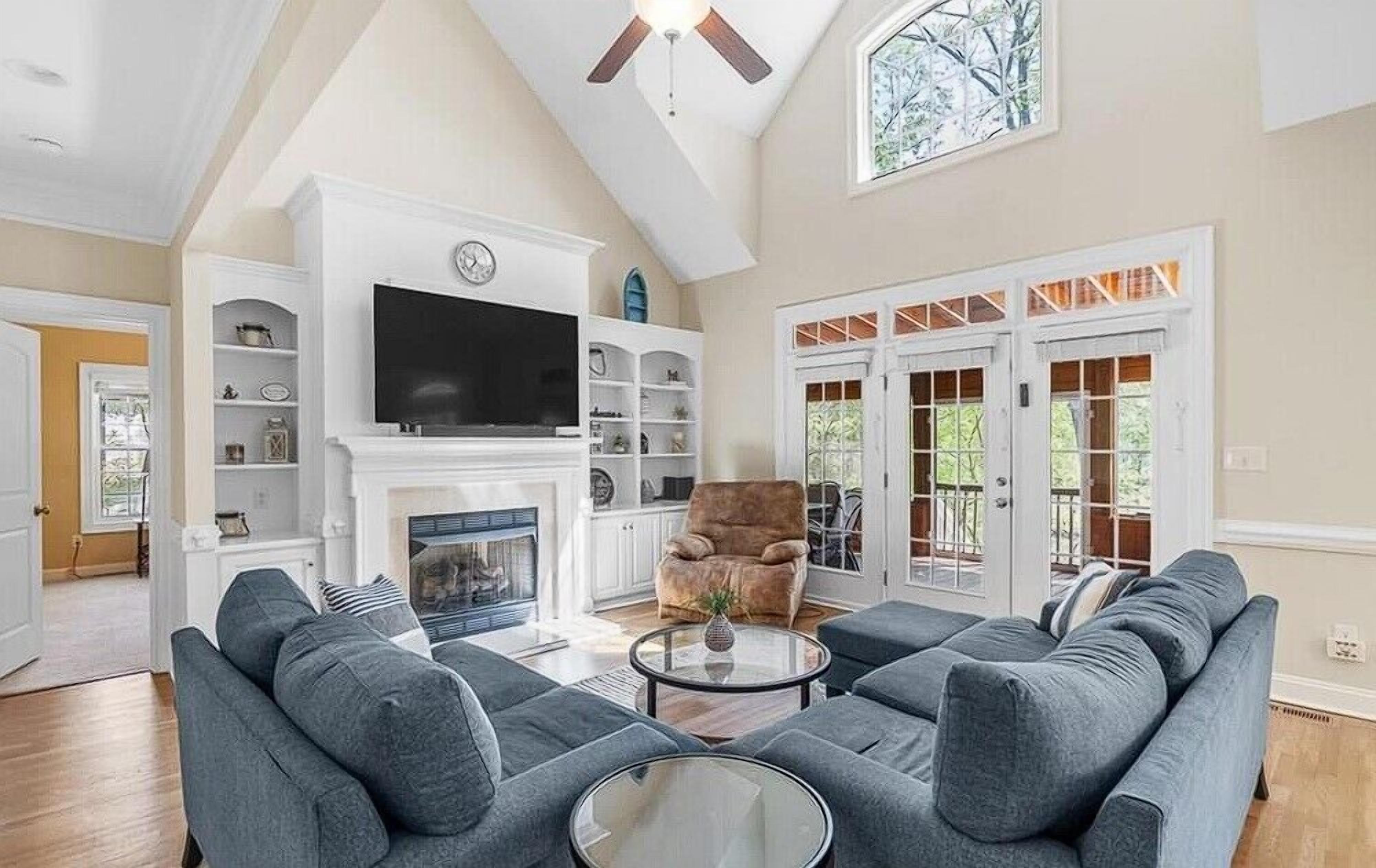 A living room with a sectional sofa, a fireplace, a television, and a ceiling fan.