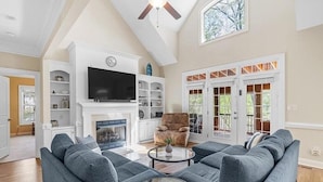 A living room with a sectional sofa, a fireplace, a television, and a ceiling fan.