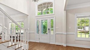 A spacious foyer with a wooden floor, white walls, and a staircase with white railings.