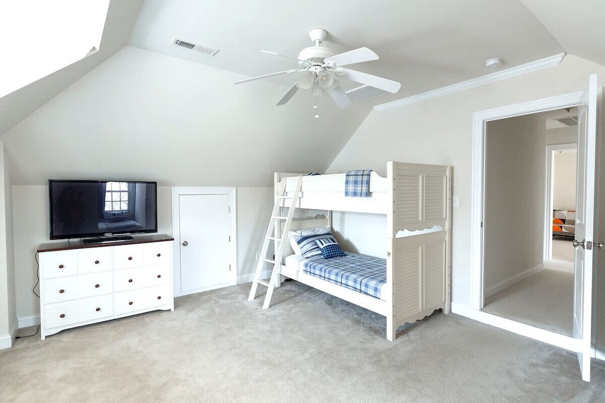 Een slaapkamer met een stapelbed, een televisie op een dressoir en een plafondventilator.