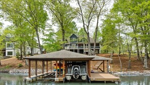 A dock with a covered area, a house in the background, and a body of water.