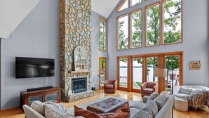 Un salón amplio con chimenea de piedra, ventanas grandes y un televisor.
