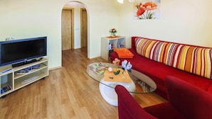 A living room with a flat-screen TV, a red sofa, a glass coffee table, and a bookshelf. - Bungalow on Lake Klopein With Garden (Sankt Kanzian am Klopeiner See)