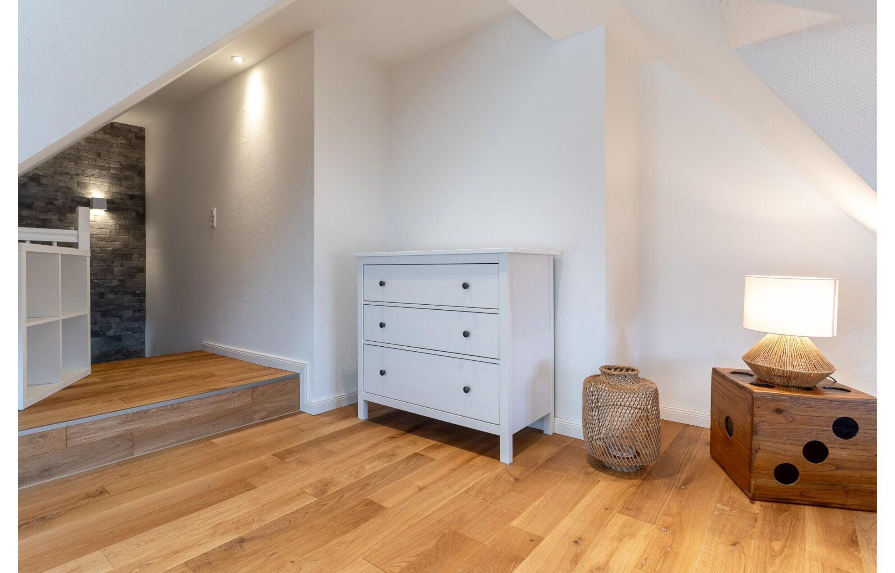 A room with a white dresser, a lamp, a woven basket, and a wooden block with holes.