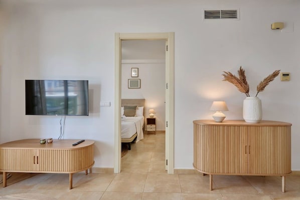 A hotel room with a TV, a round wooden cabinet, a bedside table with a lamp, and a bed with a headboard.