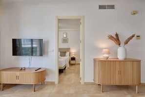 Ein Hotelzimmer mit Fernseher, einem runden Holzkabinett, einem Nachttisch mit Lampe und einem Bett mit Kopfteil.