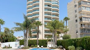 Una piscina rodeada de palmeras y sillas de descanso, con un edificio alto al fondo.