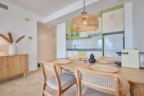 Eine moderne Küche mit Essbereich, ausgestattet mit einem Holztisch, gewebten Stühlen und einer Pendelleuchte.