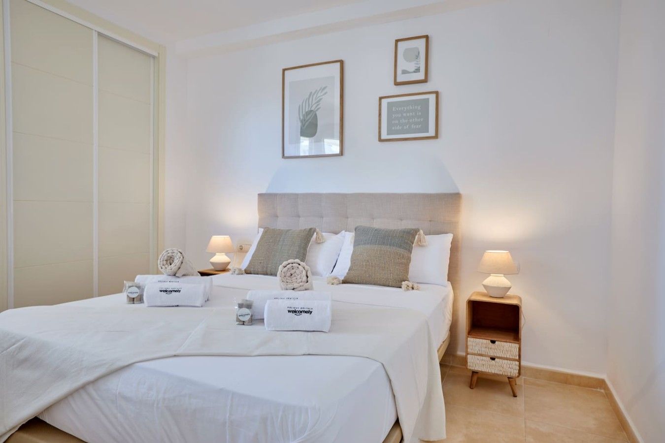 A hotel room with a bed, two bedside tables, a nightstand, a wall with framed pictures, and a door.