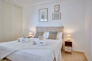 Habitación de hotel con cama, dos mesitas de noche, una mesita auxiliar, una pared con cuadros enmarcados y una puerta.
