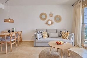 Ein Wohnzimmer mit einer Couch, einem runden Couchtisch und einem Essbereich mit Tisch und Stühlen.