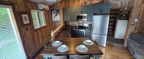 A compact kitchen with wooden walls, a dining table set with plates, a microwave, a refrigerator, and a window with blinds.