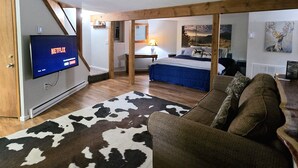 A cozy living room with a television, a cowhide rug, a sofa, and a bed in the background. - New Kitchen! ‖ Hot Tub coming August 7th! ‖ 2 Mins to Slopes ‖ Paved Road Access (Beech Mountain)