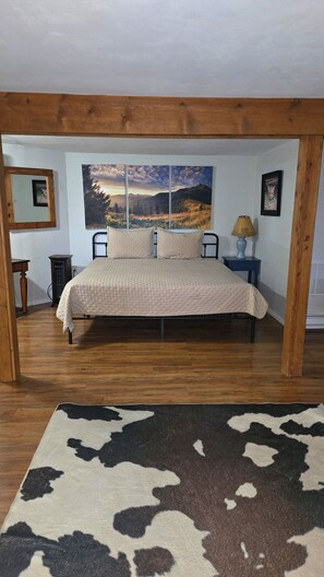 A bedroom with a bed, a nightstand, a lamp, and a large window.