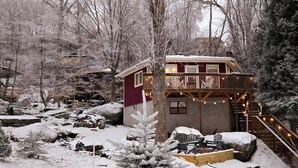 A cabin with a deck, surrounded by snow-covered trees and rocks. - New Kitchen! ‖ Hot Tub coming August 7th! ‖ 2 Mins to Slopes ‖ Paved Road Access (Beech Mountain)