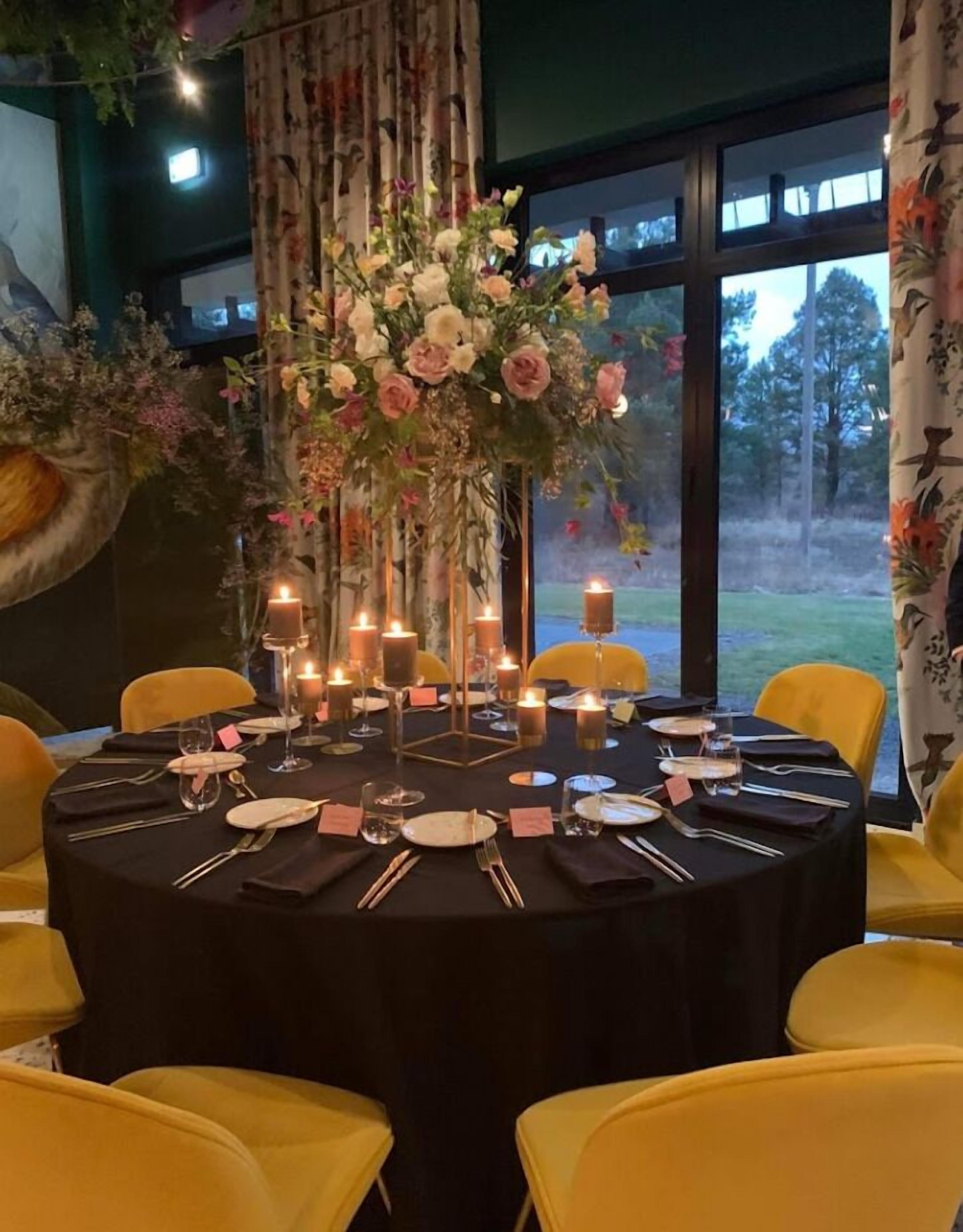 A round dining table set with yellow chairs, candles, and a floral centerpiece.