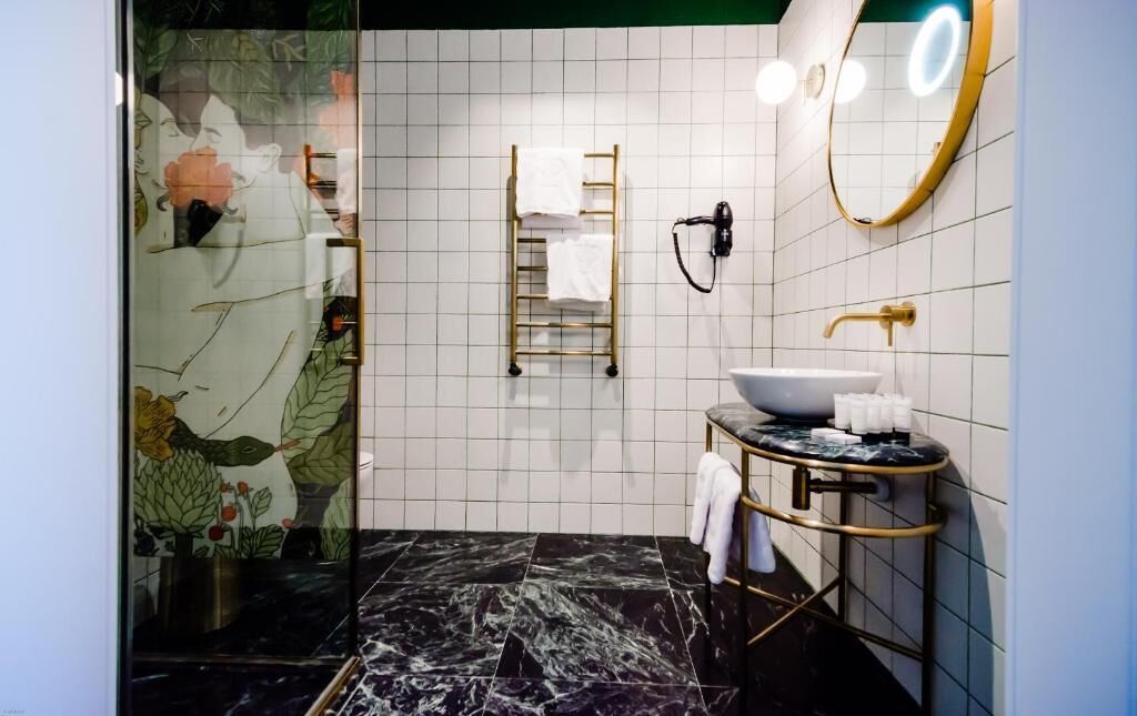 Un baño con piso de mármol negro, lavamanos blanco con detalles dorados, toallero y espejo con iluminación.