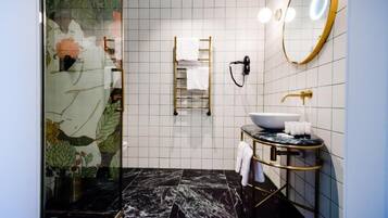 Un baño con piso de mármol negro, lavamanos blanco con detalles dorados, toallero y espejo con iluminación.