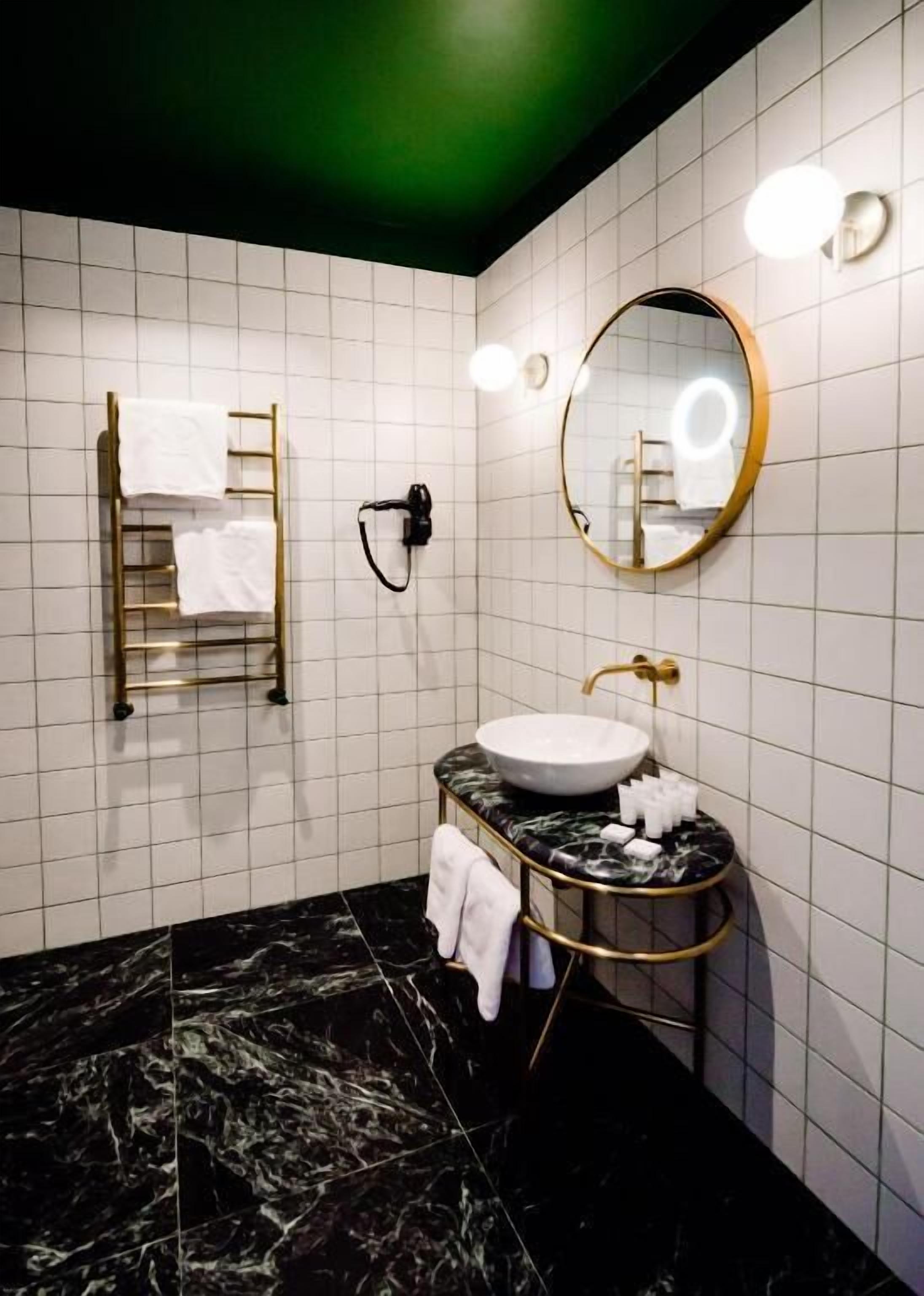 Un baño moderno con suelo de mármol, toallero dorado, espejo redondo y lavabo blanco.