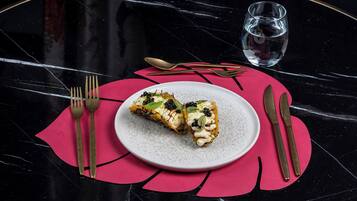 Un plato de comida sobre una mesa de mármol con un camino de mesa rojo, acompañado de cubiertos y un vaso de agua.
