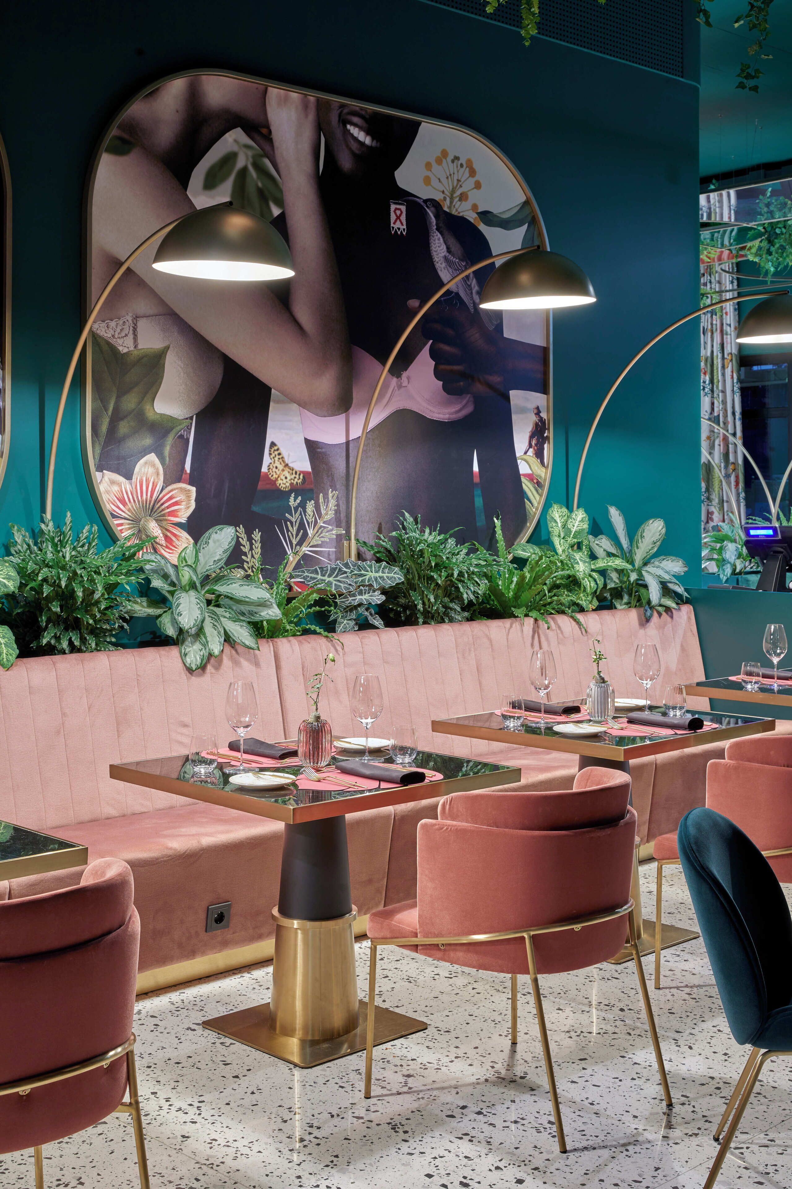 Un restaurante con una zona de asientos en una cabina rosa, mesas con sillas y un espejo grande con una pintura floral.