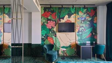 Una habitación con un amplio mural floral, un televisor de pantalla plana, un escritorio, dos sillas y una cama.