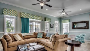 A spacious living room with a beige sectional sofa, a round coffee table, and a teal accent chair.