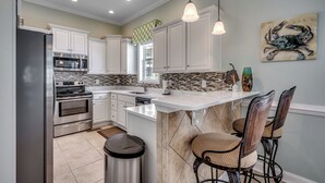 A modern kitchen with white cabinets, stainless steel appliances, a marble island, and pendant lighting.