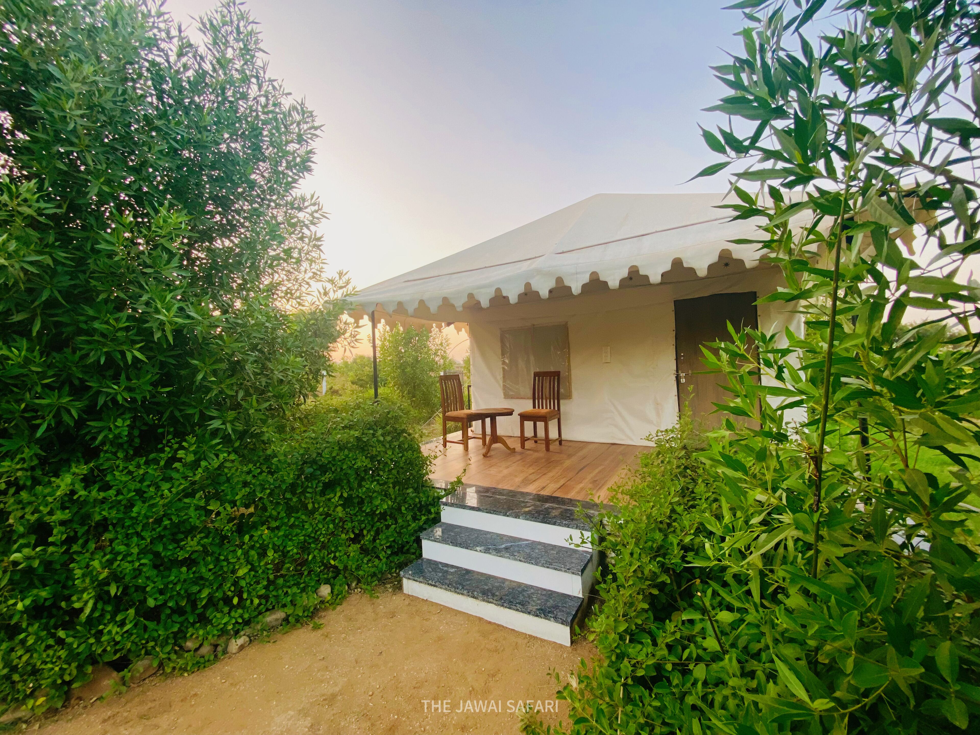 A tented structure with a wooden deck, two chairs, and a small table.