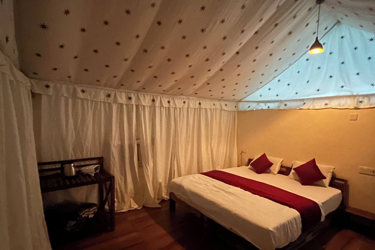 A tent-style room with a bed, curtains, a hanging light, and a wooden bench.