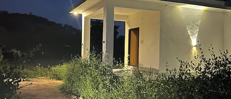 Ein modernes Haus mit überdachter Veranda, einem Feldweg, der zum Eingang führt, und umgebender Bepflanzung.
