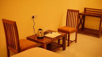 A small wooden table with a kettle and cups, two wooden chairs with cushions, and a power outlet on the wall.