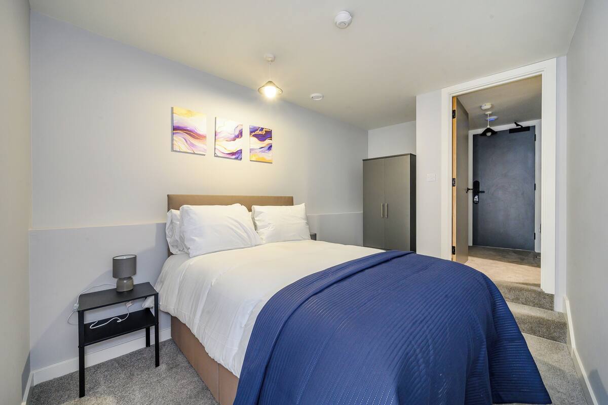 A bedroom with a bed, a nightstand, a wardrobe, and a door leading to a bathroom.